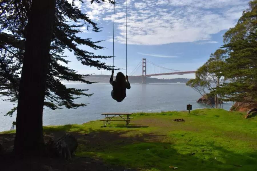 一个女人在树上荡秋千，俯瞰金门大桥. 贝博体彩app，加利福尼亚.